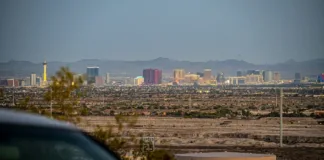 Výlety z Las Vegas: parky, časy i ceny 2026 Pohled z okna jedoucího auta - silnice vedoucí z Las Vegas do pouště s městem viditelným v zpětném zrcátku