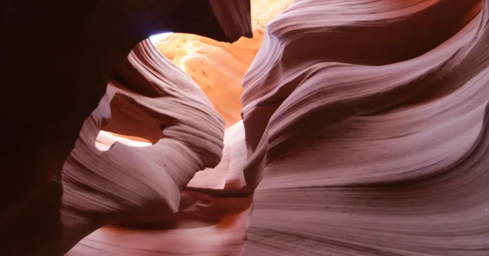 Návštěvníci procházejí úzkým slot canyonem se stěnami vysoko nad hlavami, v poledním slunci